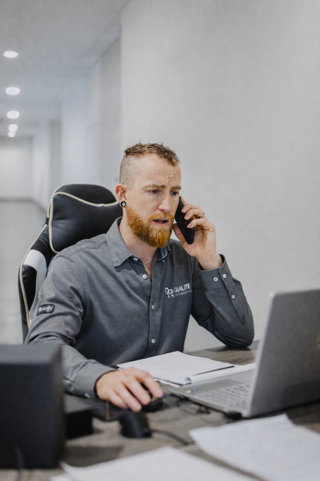 Technicien de Qualité Réfrigération parlant au téléphone dans un bureau tout en travaillant sur un ordinateur portable.