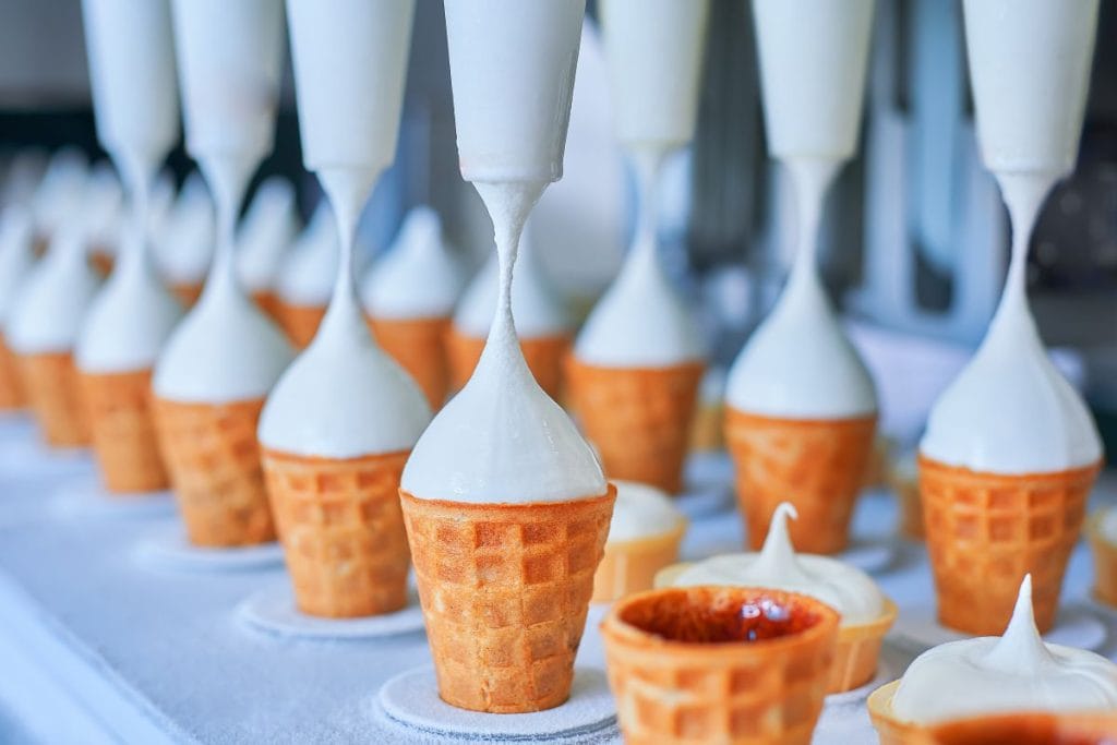 Cornets de crème glacée en gaufrette en cours de remplissage automatique avec une crème glacée blanche onctueuse