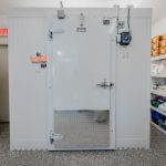Porte d'une chambre froide blanche dans une cuisine professionnelle avec étagères remplies de fournitures alimentaires
