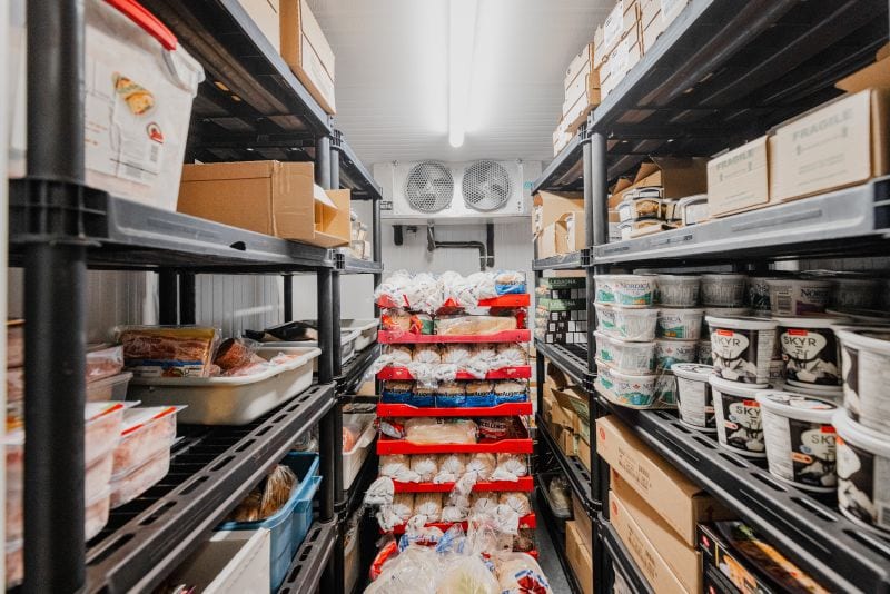 Salle froide avec étagères métalliques remplies de produits alimentaires emballés, y compris des yogourts et du pain
