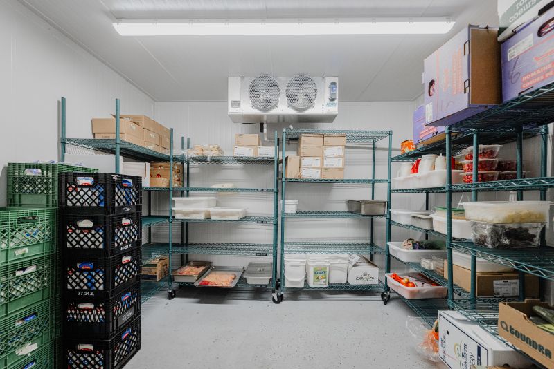 Chambre froide industrielle avec étagères métalliques remplies de boîtes en carton, caisses plastiques et contenants alimentaires