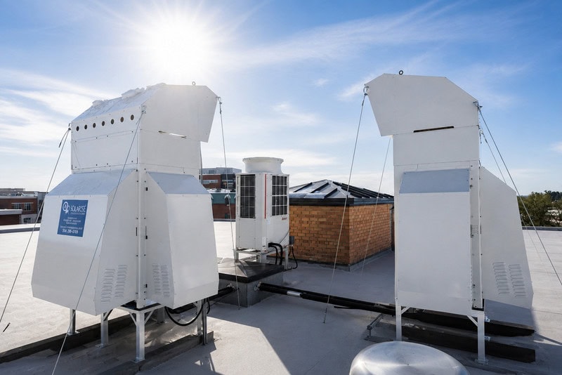 Deux unités de ventilation industrielle blanches installées sur un toit plat sous un ciel dégagé avec le soleil brillant