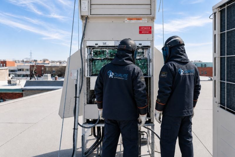 Techniciens en uniforme réparant une unité de climatisation Hitachi sur un toit urbain par une journée ensoleillée