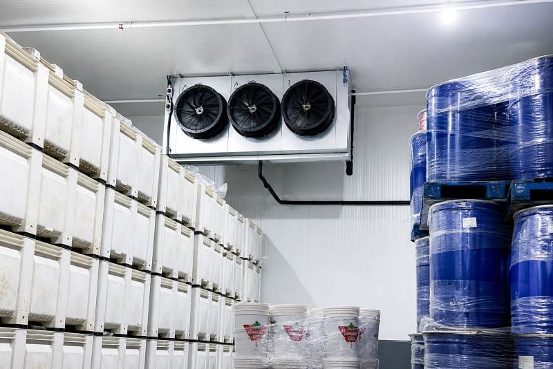 Entrepôt frigorifique avec conteneurs blancs et fûts bleus empilés et système de ventilation au plafond